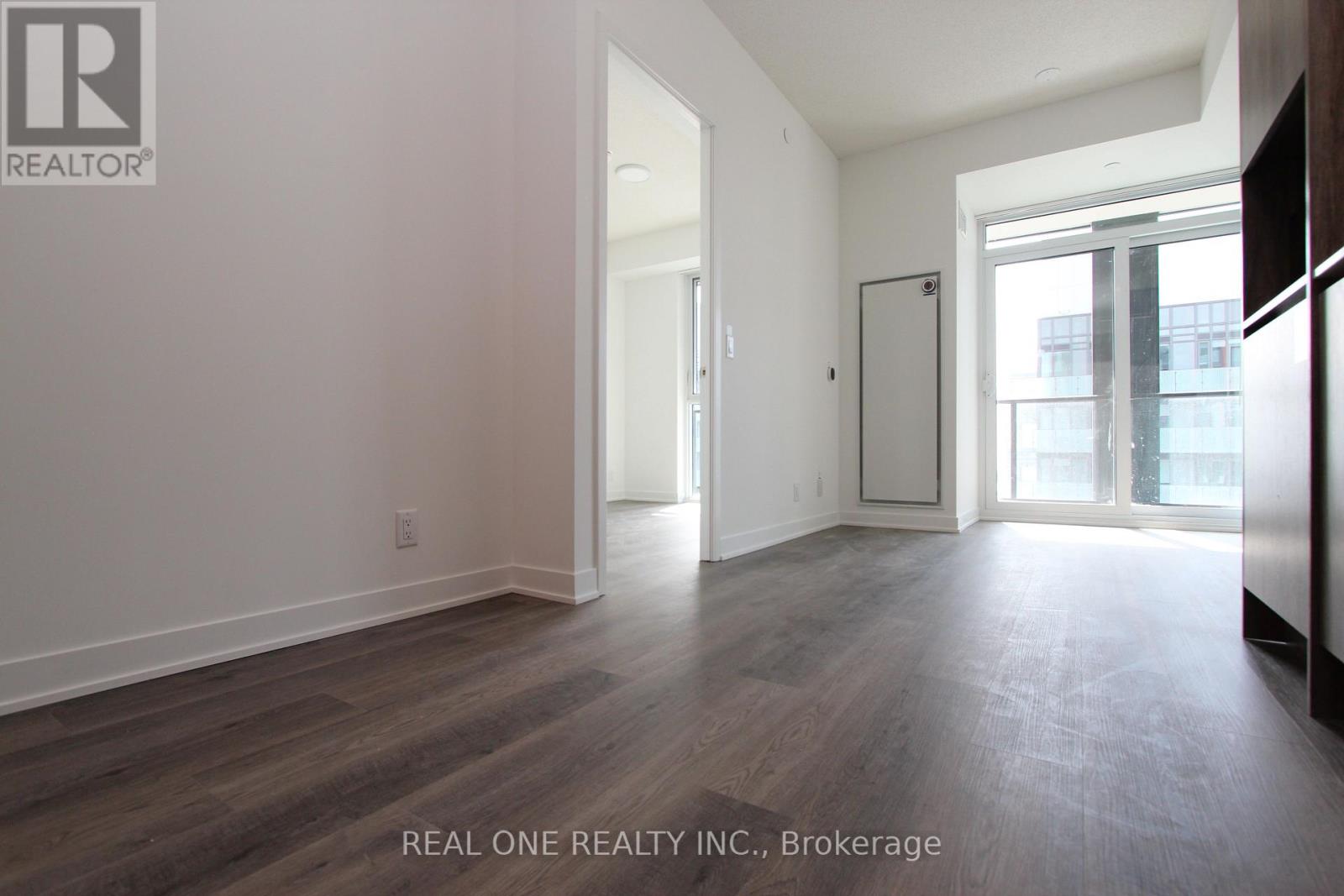 A spacious room with wooden flooring and white walls, part of a real estate listing.