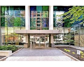 The image shows a modern building entrance with glass walls and a concrete structure.