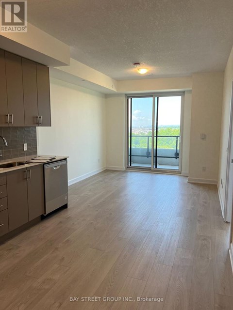 A spacious room with wooden flooring and a kitchen area with a dishwasher and a window overlooking a balcony.