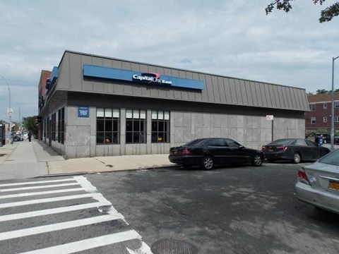 A black car is parked in front of a Capital One bank.