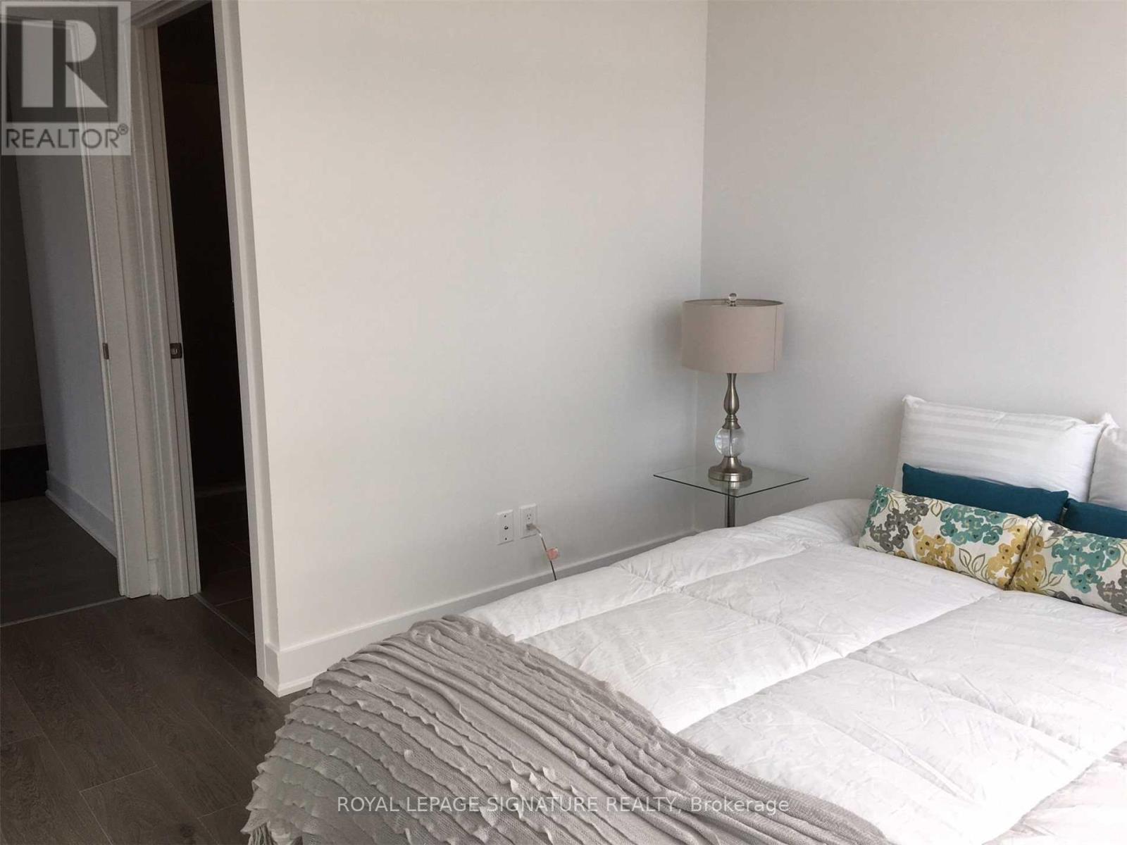 A bedroom with a white bed and a lamp on a side table.