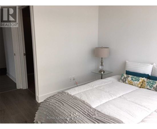 A bedroom with a white bed and a lamp on a side table.