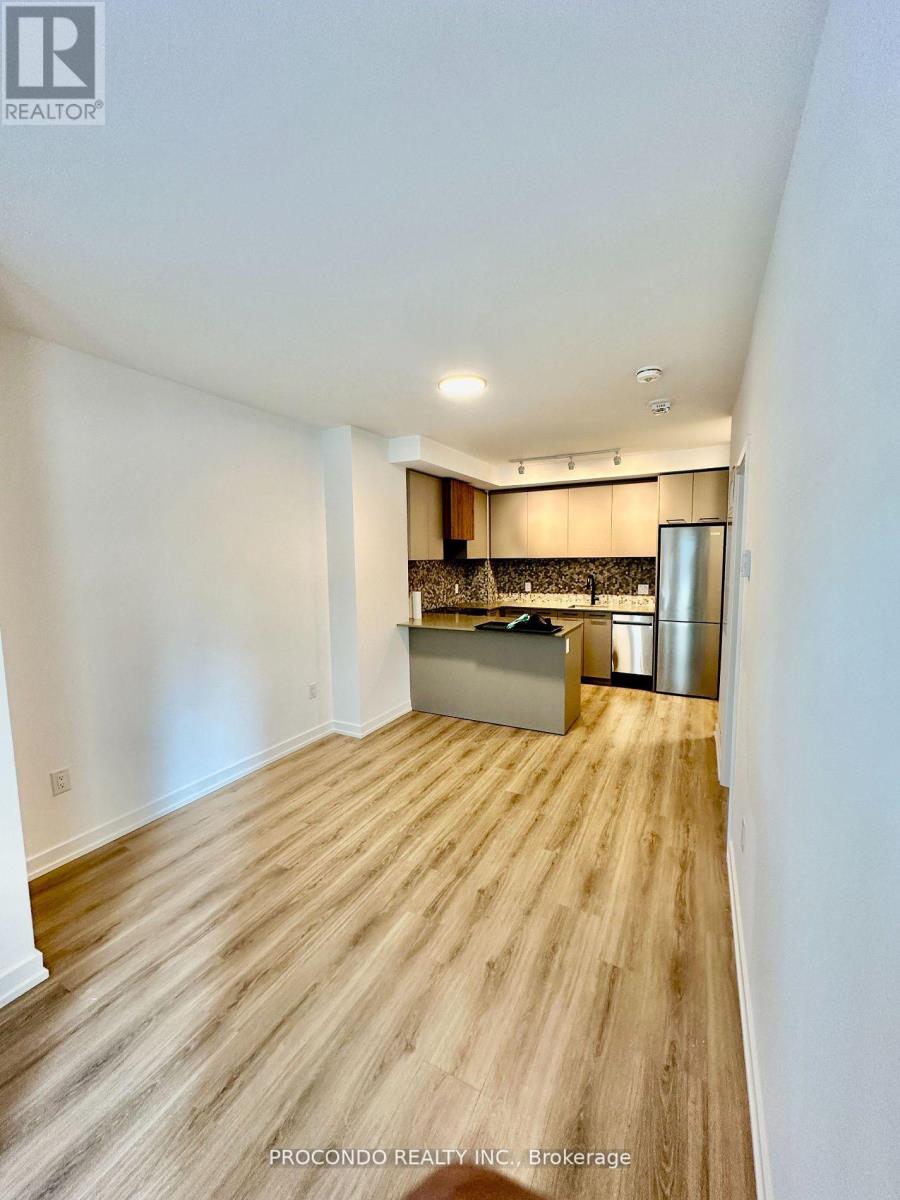 A kitchen area with wooden flooring and a stainless steel refrigerator.