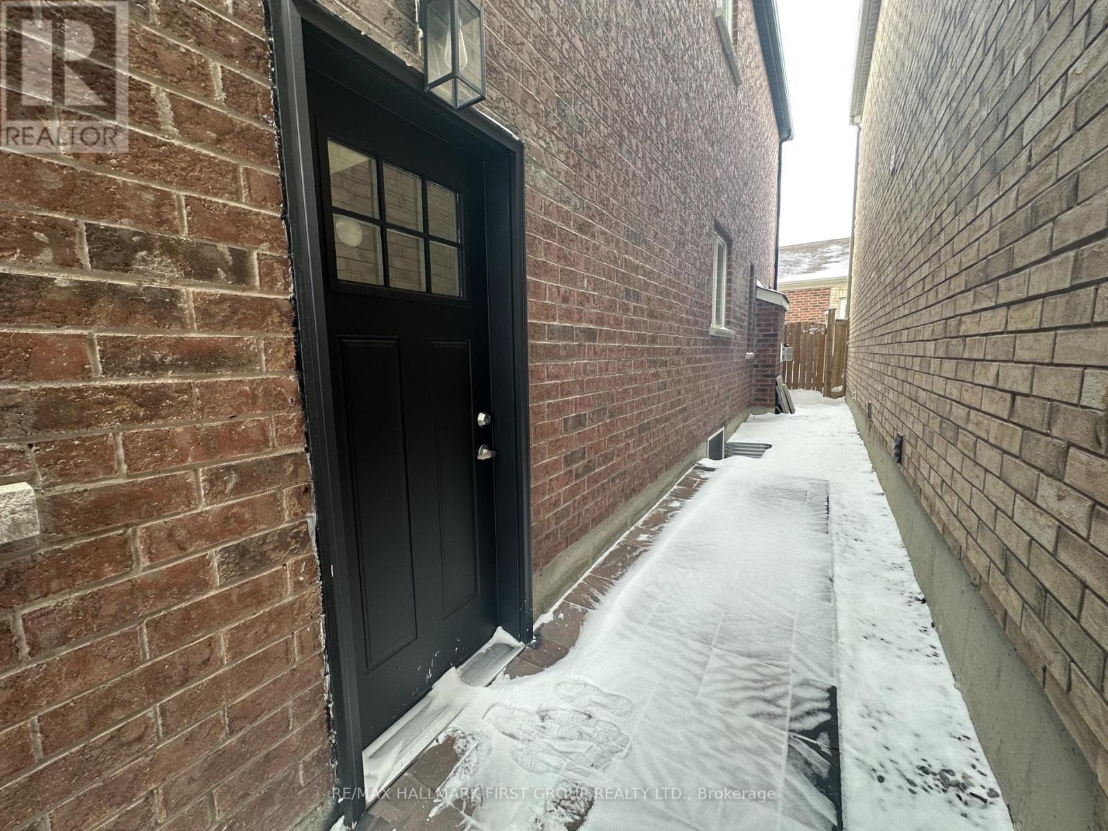 A snow-covered alley with a black door and brick walls.