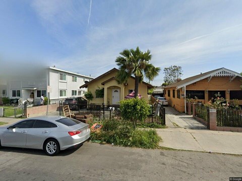 A silver car is parked in front of a house with a palm tree in the front yard.