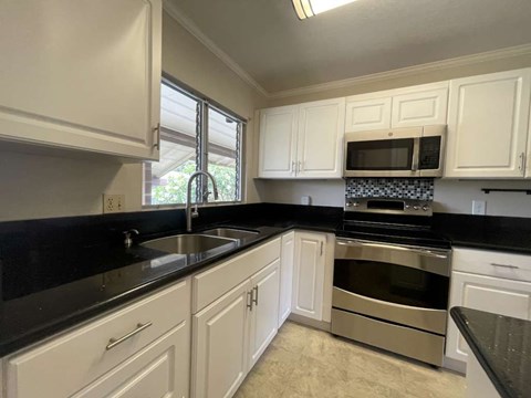 A kitchen with white cabinets and black countertops.