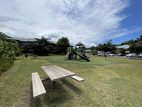 A picnic table is in the foreground of a park with a playground in the background.
