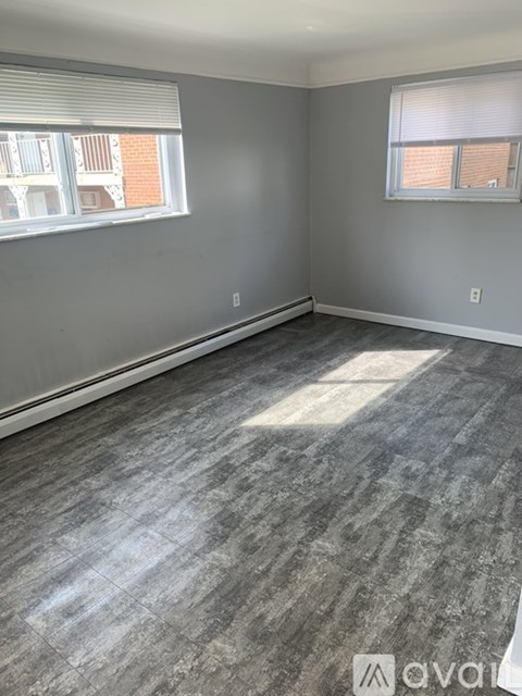 A room with grey flooring and two windows.