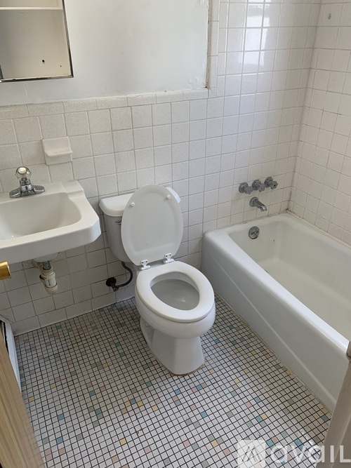 A white toilet is in a bathroom with a white sink and a white bathtub.