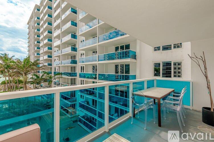 A balcony with a table and chairs overlooks a pool and a building.