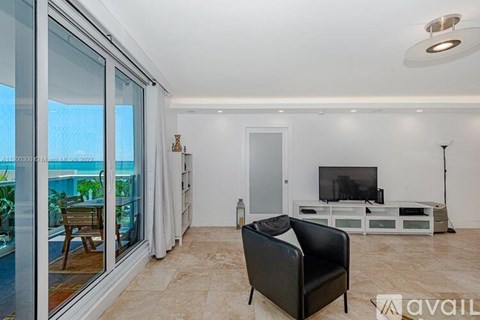 A black leather chair is in the middle of a living room with a television and a glass door leading to a balcony.
