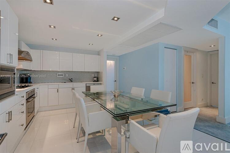 A modern kitchen with white chairs and a glass table.