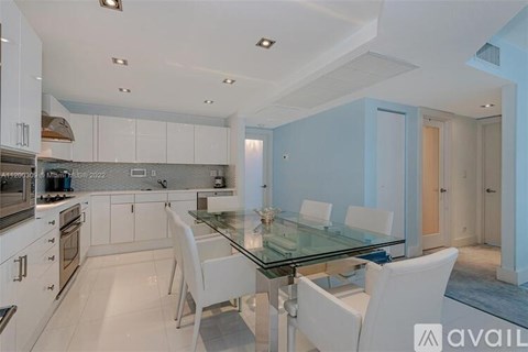 A modern kitchen with white chairs and a glass table.