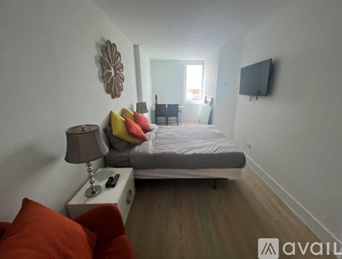 A bedroom with a bed, a lamp, a chair, and a television mounted on the wall.