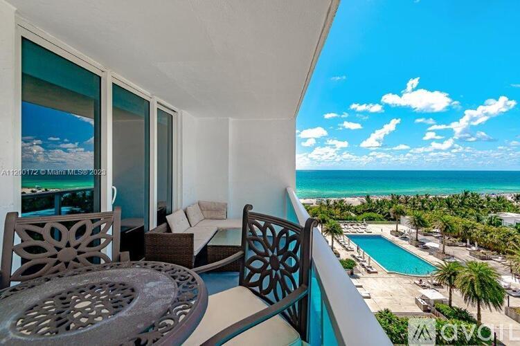 A balcony with a table and chairs overlooking a pool and beach.