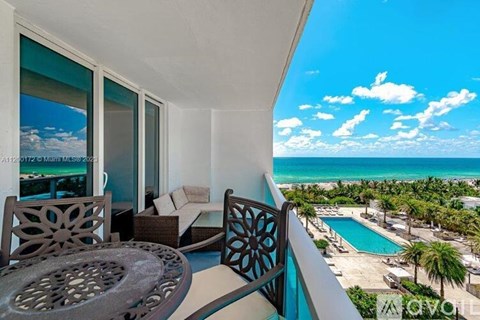 A balcony with a table and chairs overlooking a pool and beach.