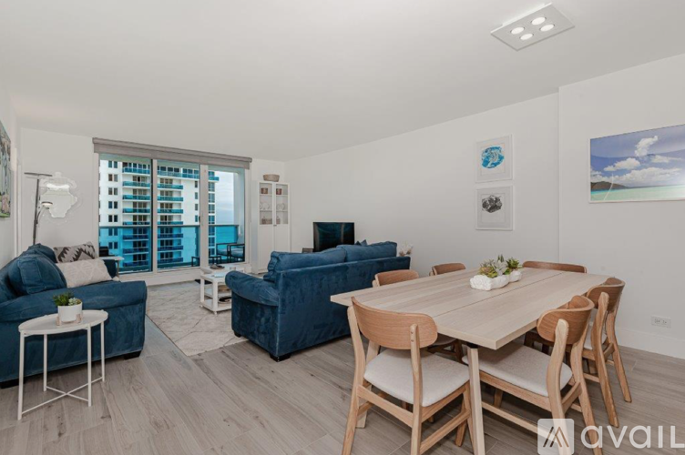 A living room with a blue couch, a white coffee table, and a wooden dining table with chairs.