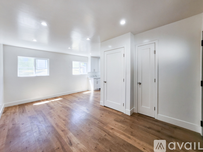 A room with wooden floors and white walls, with three doors and two windows.