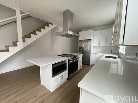 A modern kitchen with white appliances and a staircase in the background.