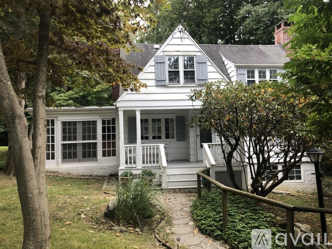 A white house with a porch and a tree in front.