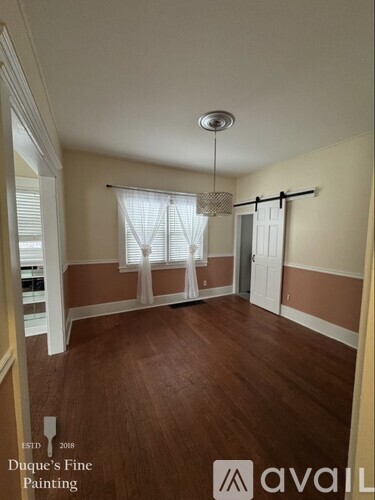 A room with a window covered by white curtains and a chandelier hanging from the ceiling.