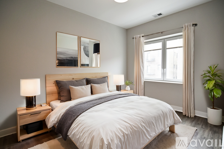 A bedroom with a large bed, a nightstand with a lamp, and a plant.