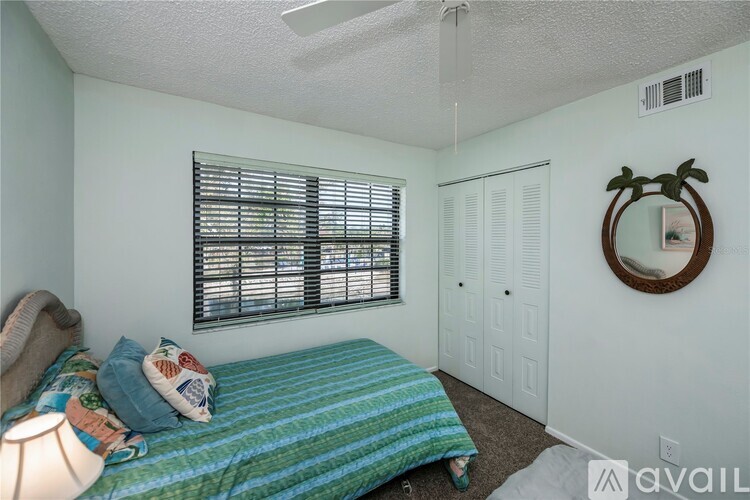 A bedroom with a bed, a window with blinds, a round mirror, and a rug on the floor.