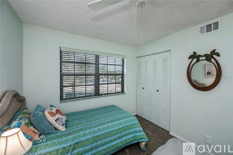 A bedroom with a bed, a window with blinds, a round mirror, and a rug on the floor.
