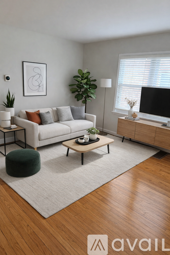 A living room with a white couch, a green ottoman, a wooden coffee table, and a TV on a cabinet.
