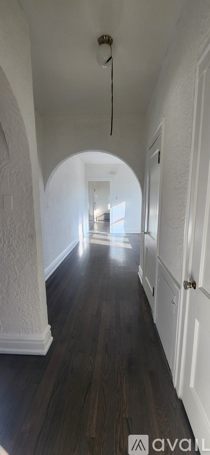 A long hallway with arched doorways and wood floors.