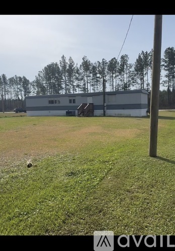 A large building with a grey roof is surrounded by a grassy field.