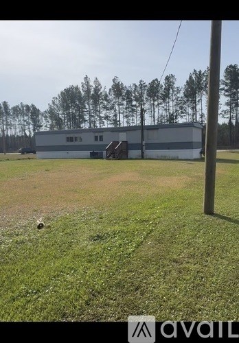 A large building with a grey roof is surrounded by a grassy field.