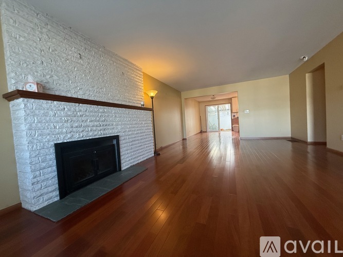 A room with a white brick fireplace and wooden floors.