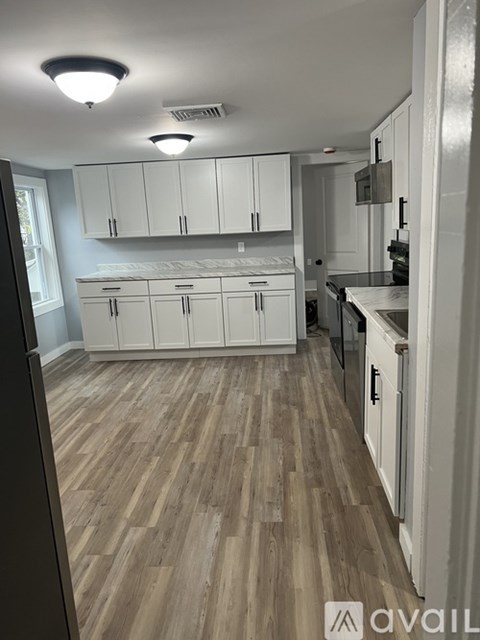 A kitchen with white cabinets and wooden flooring.