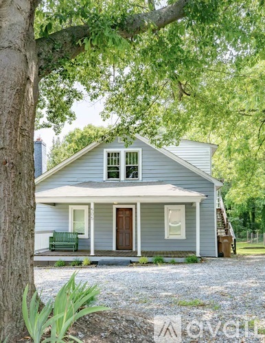 A small house with a porch and a tree in front.