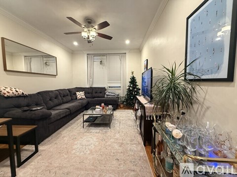 A living room with a black couch, a coffee table, a ceiling fan, and a painting on the wall.