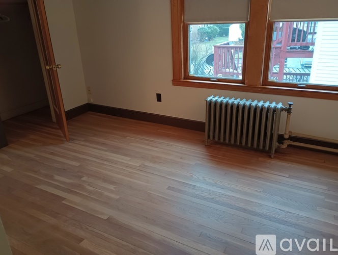 A room with wooden flooring and a window with a view of a red building.