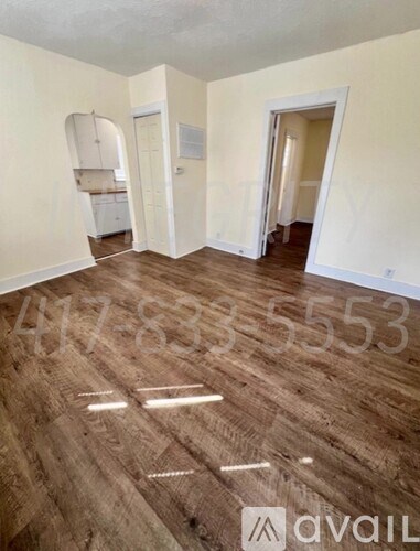 A room with wooden flooring and white walls, with a doorway leading to another room.