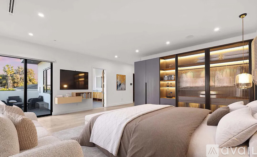 A modern bedroom with a large bed and a balcony overlooking trees.