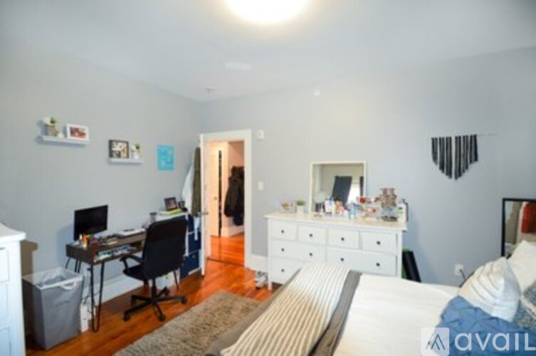 A bedroom with a white bed, a desk with a computer, and a dresser with a mirror.