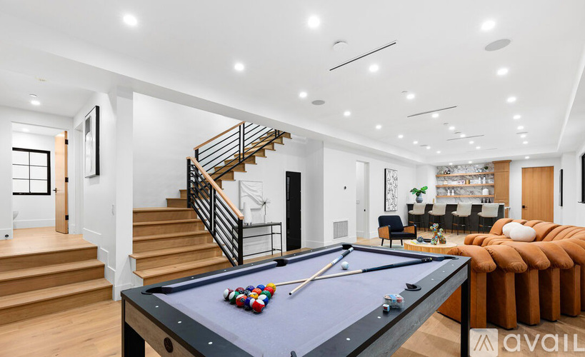 A pool table is in the middle of a room with a staircase and a couch.