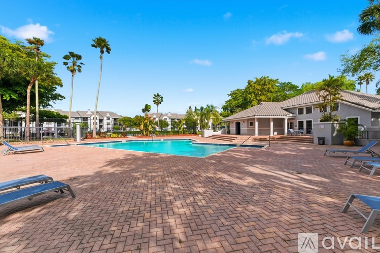 A large outdoor swimming pool surrounded by a brick patio and lounge chairs.