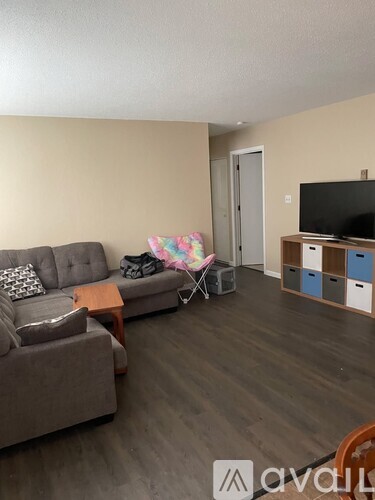 A living room with a grey couch, a wooden coffee table, a television, and a chair with a colorful cushion.