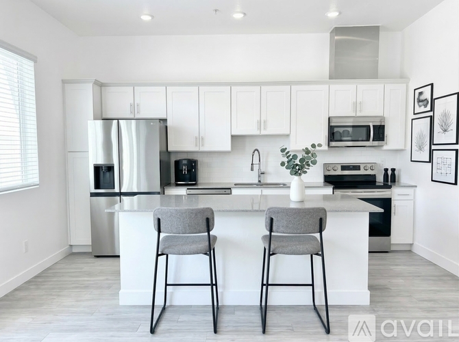 A modern kitchen with a white island and two grey chairs.