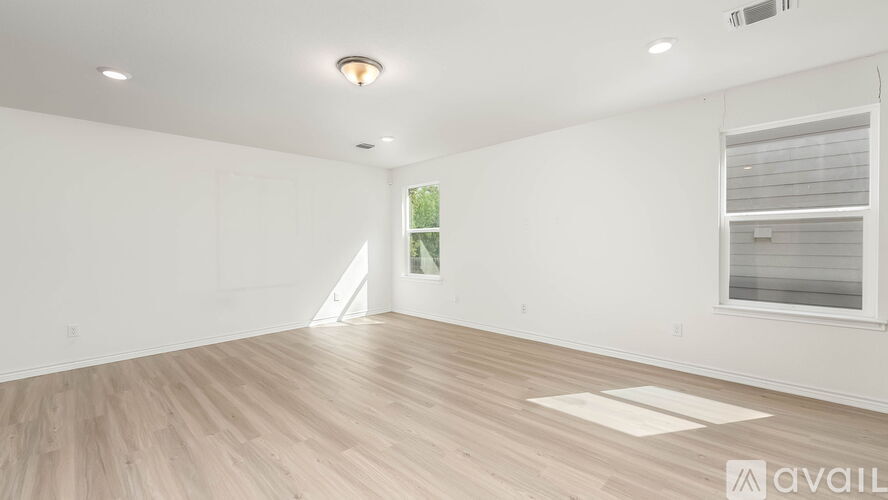 A spacious room with wooden flooring and a window with blinds.