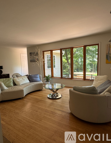 A living room with a white couch, a glass coffee table, and a window with blinds.