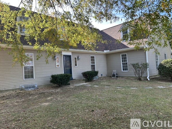 A house with a grey siding and a black door is surrounded by a grassy area.