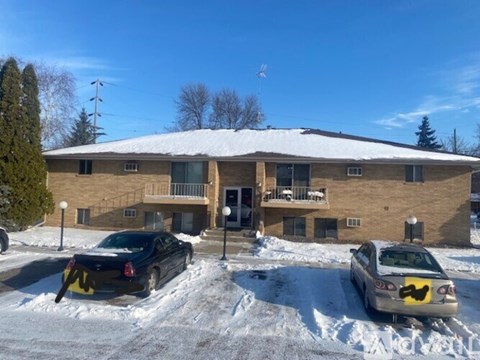 Two cars are parked in front of a building with snow on the ground.