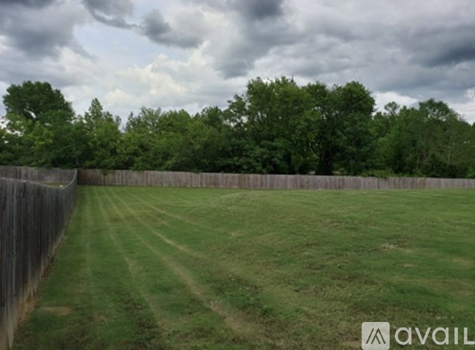 A grassy field with a fence and trees in the background.