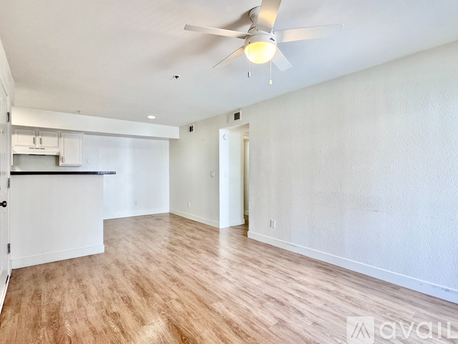 A spacious room with a ceiling fan and light fixture, hardwood flooring, and white walls.